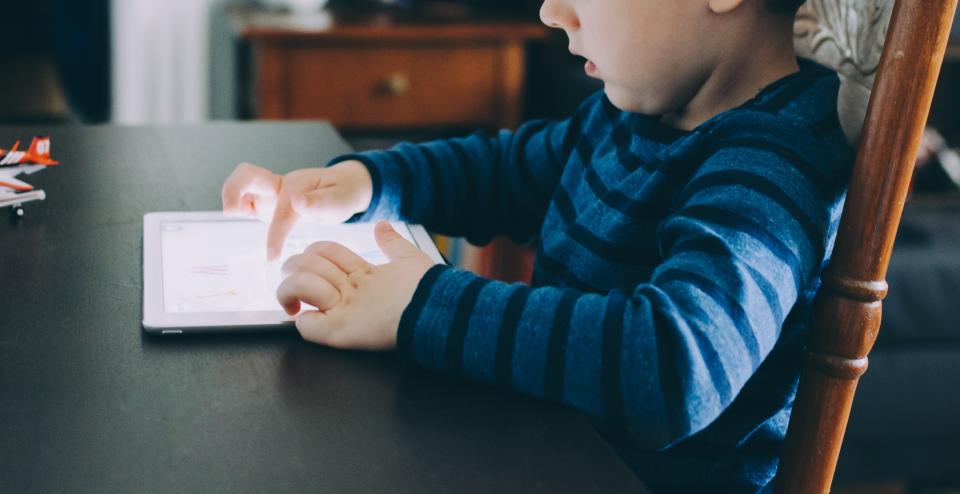 Et barn i stribet trøje spiller på en iPad ved et bord